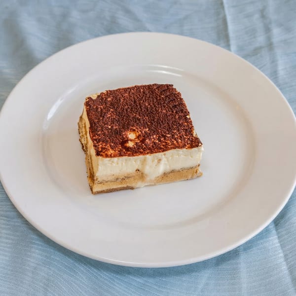A slice of tiramisu with cocoa powder on top, served on a white plate.
