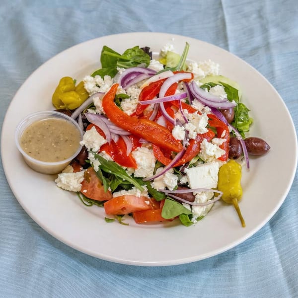 A vibrant Greek salad with feta, red onions, bell peppers, olives, and dressing on a white plate.