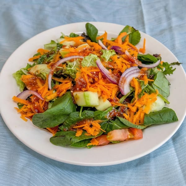 A fresh garden salad with mixed greens, shredded carrots, red onions, cucumbers, and tomatoes.