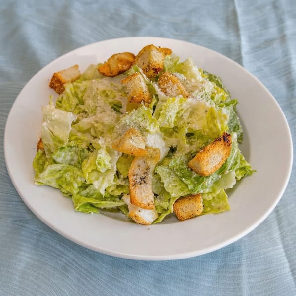 A white plate holds a Caesar salad with crisp romaine lettuce, croutons, and grated cheese.