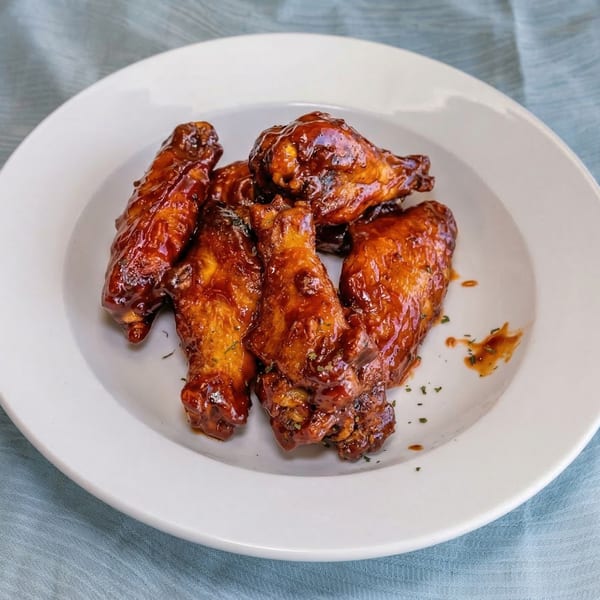 A white plate holds several glistening, dark brown chicken wings coated in a rich sauce.