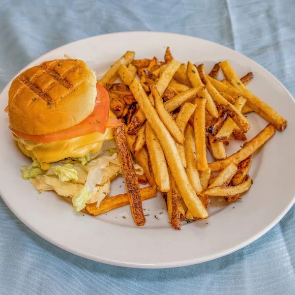 A cheeseburger with lettuce and tomato, served with a side of golden french fries on a white plate.